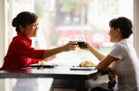 Two women at cafe, sitting face to face, toasting with drinks - Alex Microstock02