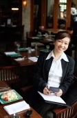 Businesswoman in restaurant, holding pen and folder, smiling - Alex Mares-Manton