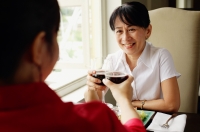 Two women at restaurant, sitting face to face, toasting with wine glasses - Alex Microstock02