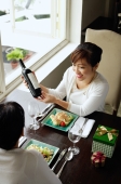Women in restaurant, food on the table, one woman holding bottle of wine - Alex Microstock02
