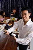 Man opening bottle of wine, smiling at camera, people in the background - Alex Microstock02