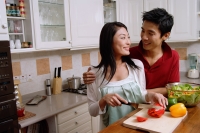 Couple in kitchen, smiling at each other, woman chopping vegetables - Alex Microstock02
