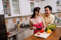 Couple in kitchen, woman chopping vegetables, looking over shoulder to smile at man - Alex Microstock02