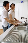 Couple in kitchen, woman washing dishes, man standing behind her - Alex Microstock02