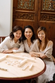 Three women sitting next to each other, at mahjong table, smiling - Alex Microstock02
