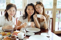 Three women sitting side by side in cafe, smiling at camera - Alex Microstock02