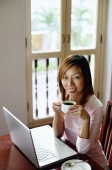 Woman using laptop, holding cup, smiling at camera - Alex Microstock02