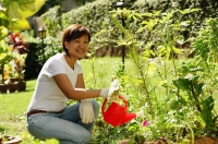 Woman watering plants in garden, smiling at camera - Alex Microstock02