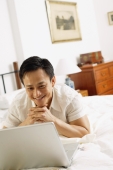 Man in bedroom, looking at laptop, hands clasped, under chin - Alex Microstock02