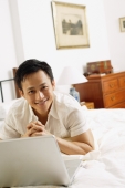Man in bedroom, using laptop, hands clasped, looking at camera - Alex Microstock02