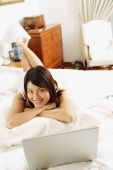 Woman in bedroom, lying on bed, laptop open in front of her - Alex Microstock02