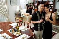 Couple at home, holding wine glasses, smiling at camera, people in the background - Alex Microstock02