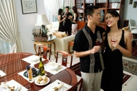 Couple at home, holding wine glasses, smiling at each other, people in the background - Alex Microstock02