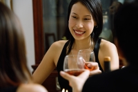 Woman smiling, holding wine glass, toasting with person sitting opposite - Alex Microstock02