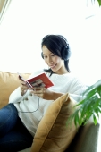 Woman sitting on sofa, wearing headphones, looking at CD case - Alex Microstock02