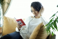 Woman sitting on sofa, wearing headphones, holding CD case - Alex Microstock02