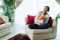 Woman sitting in living room, hugging pillow, smiling at camera - Alex Microstock02
