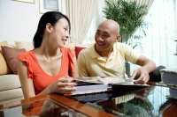 Couple at home in living room, looking at each other, photo album in front of them - Alex Microstock02
