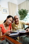Couple at home in living room, photo album in front of them, smiling at camera - Alex Microstock02