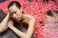 Woman leaning at edge of tub filled with floating rose petals - Alex Mares-Manton