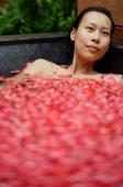 Woman in tub filled with floating rose petals, looking away - Alex Mares-Manton
