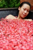 Woman in tub filled with floating rose petals, looking at camera - Alex Mares-Manton