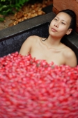 Woman relaxing in tub with floating rose petals - Alex Mares-Manton