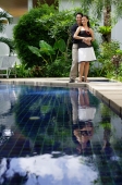 Couple standing by swimming pool, man embracing woman, both smiling at camera - Alex Mares-Manton