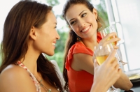 Two women holding wine glasses, smiling at each other - Alex Mares-Manton