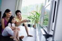 Family of three in front of TV, man pointing remote control at TV - Alex Mares-Manton