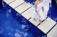 Couple walking on walkway across pool - Alex Mares-Manton