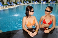Young women in swimming pool, wearing sunglasses and holding cocktails - Alex Mares-Manton