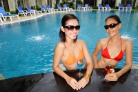 Young women in swimming pool, wearing sunglasses, smiling at camera - Alex Mares-Manton