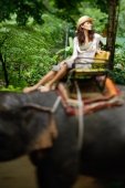 Young woman sitting on top of elephant, looking away, Phuket, Thailand - Alex Mares-Manton