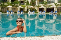 Woman in swimming pool, adjusting sunglasses, smiling - Alex Mares-Manton