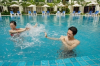 Couple in swimming pool, having water fight - Alex Mares-Manton