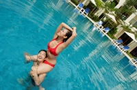 Couple in swimming pool, woman sitting on mans shoulders, looking away - Alex Mares-Manton