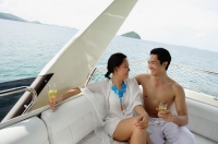 Couple sitting on stern of yacht, holding champagne glasses - Alex Mares-Manton