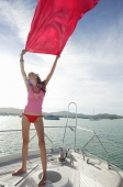 Young woman on windy boat deck, holding piece of cloth in the air - Alex Mares-Manton