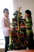 Couple decorating Christmas tree, looking at camera - Alex Microstock02