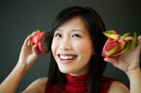 Woman holding dragon fruit halves next to her ears, smiling - Alex Microstock02