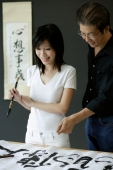 Woman holding paintbrush, looking at Chinese painting, man standing next to her - Alex Microstock02