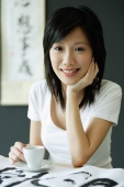 Young woman with teacup and saucer, smiling, hand on chin - Alex Microstock02