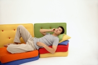 Man lying on multi-coloured sofa, listening to personal stereo - blueduck