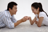 Couple lying on front, face to face, man holding womans ring finger - blueduck