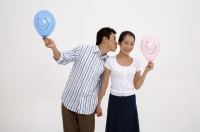 Couple holding hands, holding balloons, man leaning over to kiss woman on cheek - blueduck