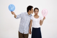 Couple holding balloons, man leaning over to kiss woman on cheek - blueduck