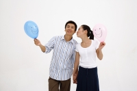 Couple holding hands, holding balloons, woman kissing man on cheek - blueduck