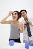 Woman applying mascara, man standing behind her, adjusting tie - blueduck