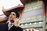 Businessman using mobile phone, standing in front of temple gate - Alex Microstock02
